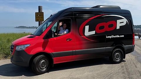 a black and ride van is parked by the ocean with a smiling driver waving