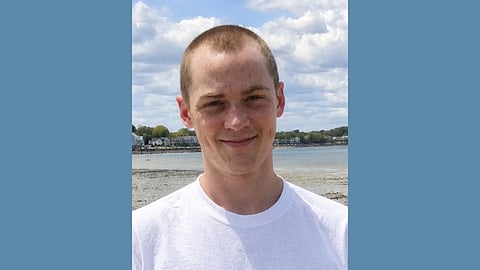 photo of a young white man in a white t-shirt with a closed mouth smile against the backdrop of a blue sky