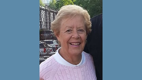 photo of a smiling older white woman with blonde har in a pink cable knit sweater