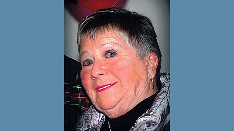 Older white woman with short silver hair wearing a black top and silver jacket smiling at the camera