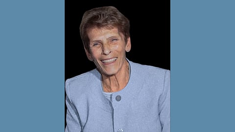 Older white woman with short brown hair wearing a pale blue suit smiles at the camera