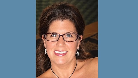 A middle aged woman with brown hair and glasses wearing a strapless dress and dangling earrings