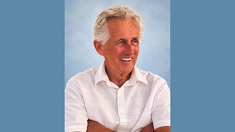 Older white man with white hair wearing a white linen shirt and smiling and looking at the distance
