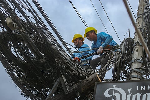 WIRE AND CABLE CLEANUP. Two workers pull the tangled pile of cords left by telecom companies on a post along Rizal St., Poblacion District, Davao City on Sunday, February 4, 2024. According to the Davao Light and Power Company workers on site, they plan to finish the cleanup of wires and cables by the end of the day.