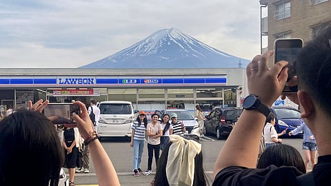 Visitors take a photo in front of a convenient store at Fujikawaguchiko town, Yamanashi prefecture, Japan, with a backdrop of Mr. Fuji on April 28, 2024.