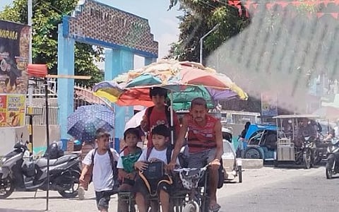 UNDER THE SUN. A large umbrella shields students from the heat as they go home riding a bike with sidecar from Buenlag Central School in Calasiao, Pangasinan on Thursday (April 25, 2024). Pangasinan has been posting over 40 degrees Celsius heat index since a few weeks ago, and local government officials have implemented various measures to lessen the impact of the high heat index to the students.
