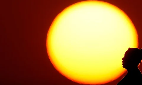 A woman is silhouetted against the setting sun as triple-digit heat indexes continue in the Midwest, Aug. 20, 2023, in Kansas City, Mo. The rate Earth is warming hit an all-time high in 2023 with 92% of last year’s surprising record-shattering heat caused by humans, top scientists calculated.