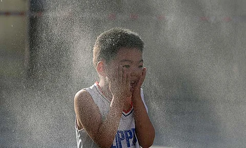 A child reacts to a mist machine as he cools off from the summer heat in Beijing, Saturday, June 15, 2024.