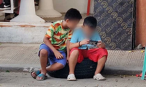 CONTRASTING VIBE. Outside a local barbershop, two young children are seen sitting on an old, abandoned wheel propped up against the curb. As they pass the time, their attention is fully absorbed in a mobile game. The scene contrasts the worn, urban surroundings with the innocence of childhood, offering a quiet moment of escape amidst the hustle and bustle of the street. However, medical experts reminded parents to limit their child’s screen time emphasizing the potential negative effects of excessive exposure to screens.