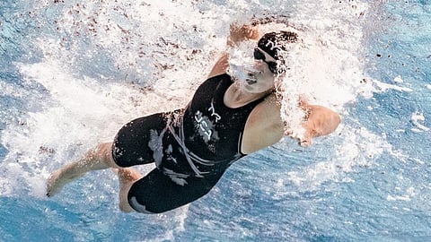 Katie Ledecky, wearing a swimming cap and goggles, powerfully swimming freestyle in a competitive swimming pool during a race, with water splashing around her.
