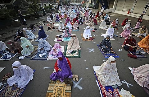 Muslim women sit spaced apart to help curb the spread of coronavirus outbreak during an Eid al-Fitr prayer marking the end of the holy fasting month of Ramadan on a street in Jakarta, Indonesia, Thursday, May 13, 2021. (AP Photo/Dita Alangkara)