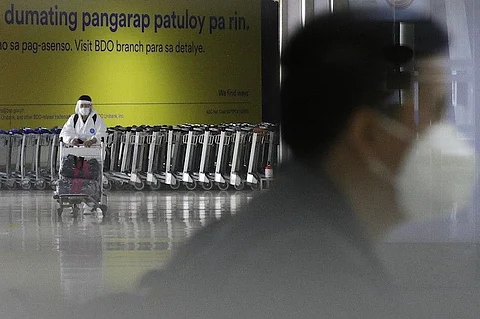 MANILA. In this photo taken in March 2021, a woman wearing a protective suit pushes a cart at the arrival area of the Ninoy Aquino International Airport. (File)