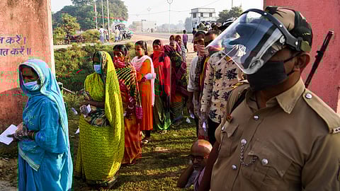 A policeman stands guard as voters queue up to cast their ballots for Bihar state assembly elections