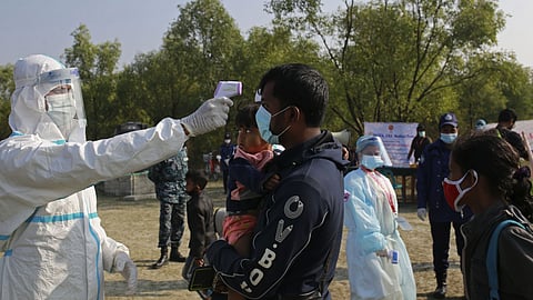 An official wearing a protective suit checks the body temperature of a man