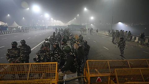 Police personnel stand guard next to barricades along a blocked highway