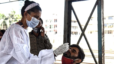 A health worker takes a swab sample from passengers arriving at a railway station in Mumbai