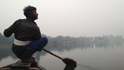 नाव पर सवार गोमती नदी में मछलियों का शिकार करता मछुआरा।