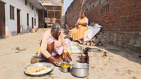 एक बुजुर्ग महिला खाना पका रही है, जबकि दूसरी बुजुर्ग महिला बंदरों को रोकने के लिए डंडा लेकर बैठी है.