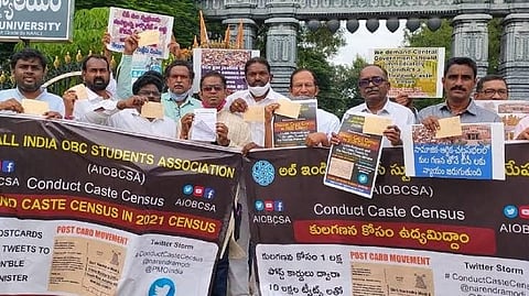 A group of protestors holding placards and postcards at Kakatiya University in Warangal, demanding a caste census. Banners from the All India OBC Students Association (AIOBCSA) call for caste enumeration and display hashtags and slogans supporting the movement.