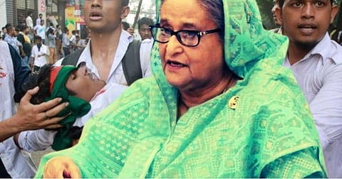 Sheikh Hasina. In the background is an injured protester being carried by fellow protesters in Bangladesh.