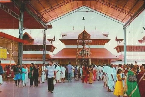 People gather at Guruvayur temple with traditional architecture, featuring a large entrance and ornate roof. The scene is lively, with visitors dressed in colorful attire, capturing a vibrant cultural setting under a clear sky.