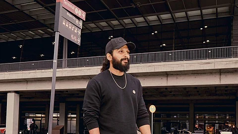 Allu Arjun in a black sweatshirt and pants standing on a pedestrian crossing outside an airport