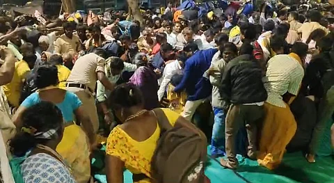 A dense crowd of people gathered closely in a chaotic manner, some bending and appearing to be in motion, at the Tirumala temple.
