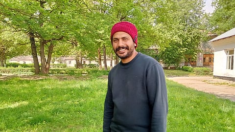 Binil wearing a red cap and posing for a photograph in a lush green field outside his home