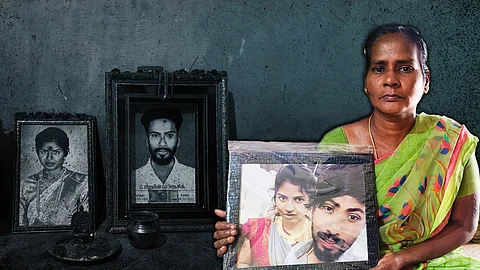 Photograph of two deceased persons, a woman and a man. A framed photograph depicting a woman in grey and pink saree and a man in white shirt, being held in the hands of a woman who in wearing a green saree.