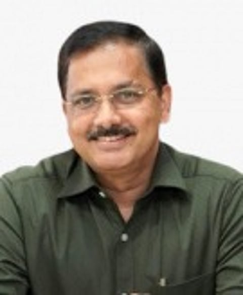 Judge AM Basheer wears an olive green shirt and spectacles and smiles at the camera.