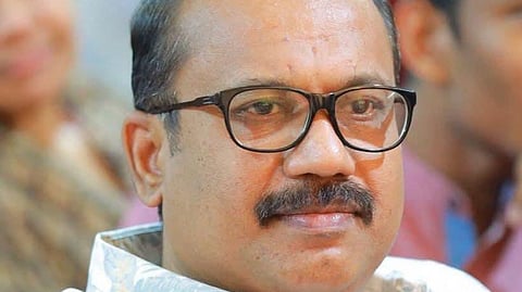 Shafi wearing glasses and a patterned shirt, seated with a composed expression