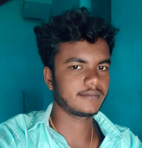 19-year-old BSc Maths Dalit student Ayyasamy in a selfie. Wearing a blue shirt and a golden chain. Standing in front of a blue wall.