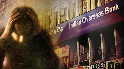 A distressed person with their hands on their head is superimposed over an image of an Indian Overseas Bank branch.
