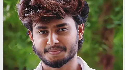 YouTuber Harsha Sai with wavy brown and black hair, a well-groomed beard, and a confident expression. He is wearing a crisp white shirt with the top buttons undone, standing against a blurred green outdoor background. His arms are crossed, and he has a slight smile on his face.