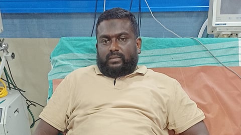 Thoufiq alias Krishnamurthy in a beige polo shirt, lying on a hospital bed.