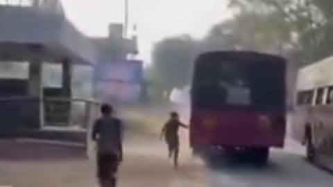 A young girl in a school uniform, wearing a school bag, chasing after a pink Tamil Nadu government bus.