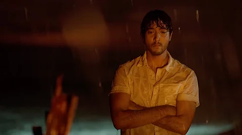 Sumukha in a scene from the film, facing the audience in a white shirt, looking distressed.