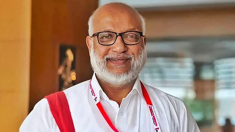 CPI(M) leader MA Baby in a white shirt with a red cloth bag slung over his right shoulder, smiling at the camera