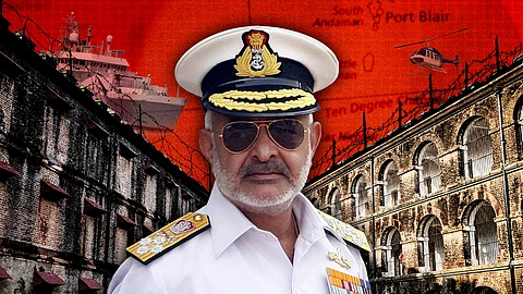 **Alt text:**
An Indian Navy officer wearing a white uniform, medals, and a peaked cap with the Indian emblem stands in the foreground. He has a stern expression and wears aviator sunglasses. In the background is a collage featuring the historic Cellular Jail in Port Blair, barbed wire, a naval ship, a helicopter, and a red-toned map of the Andaman and Nicobar Islands with "Port Blair" and "Ten Degree Channel" marked. The visual conveys themes of military presence, security, and historical significance.