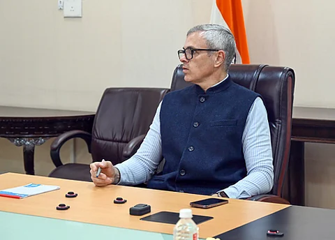 Jammu and Kashmir Chief Minister Omar Abdullah seated at a conference table, wearing a navy blue Nehru jacket over a light shirt, with the Indian flag partially visible in the background.
