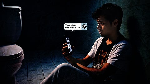 A young man sits alone on a bathroom floor at night, lit dimly by his phone screen. He looks anxious and vulnerable, clutching his phone tightly. On the screen is a message from an AI chatbot: “Take a deep breath. You’re safe.” The toilet is visible beside him, emphasising the isolation of the moment.