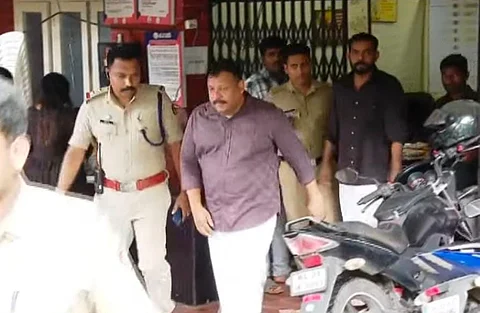 Rajesh and Akhin are being escorted by Kerala Police officers from a police station following their arrest in a cheating case