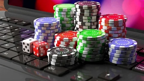 Stacks of colourful poker chips and dice placed on a laptop keyboard, symbolising online gambling platforms.
