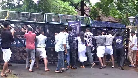 A group of SFI student protesters push against a barricaded gate at Kannur University