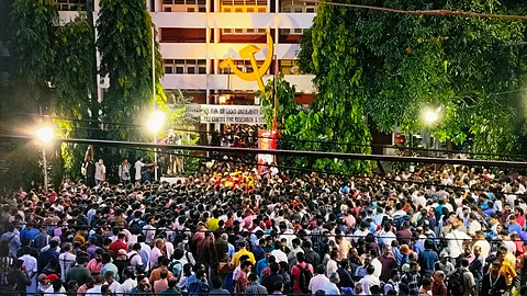 Large crowd of people gathered outside the AKG Centre in Thiruvananthapuram at dusk, under bright lights and a giant hammer-and-sickle emblem, to pay tribute to veteran CPI(M) leader VS Achuthanandan.