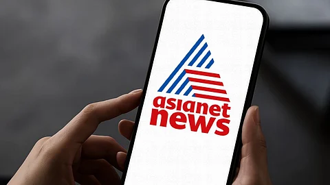 A person holding a smartphone displaying the logo of Asianet News