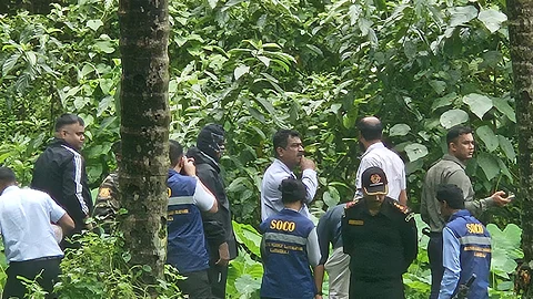 In a thick forest covered in vegetation, officials are seen examining the alleged burial sites