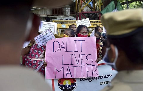 Protesters holding a sign that reads "Dalit Lives Matter" during a demonstration, with police in the foreground, highlighting caste-based discrimination issues in India.