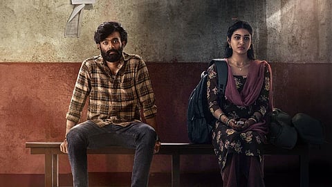 This image appears to be a promotional poster for the film Elumale. It features two characters seated on a bench in a seemingly tense or contemplative moment. The man, dressed in a plaid shirt with a beard, sits with a serious expression, while the woman, wearing traditional attire, is focused on her phone. The background gives off a gritty, emotional vibe, suggesting a narrative filled with depth and emotion. The poster conveys a sense of distance and introspection between the characters, potentially reflecting the film's theme of complex relationships.
