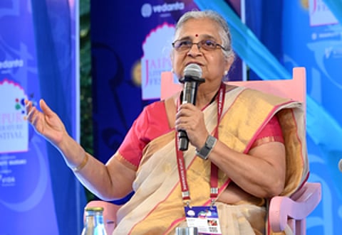 Sudha Murthy speaking at an event, mic in left hand, seated in a chair